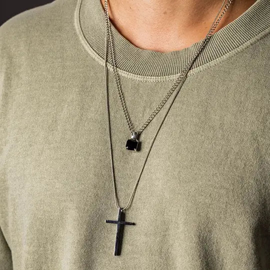 Homem com camiseta verde oliva usando colares de aço com cruz e pedra preta.