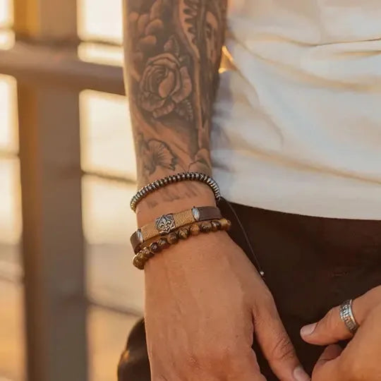 Homem com tatuagem no braço exibindo a Pulseira Brasão de Lís da Virt Design ao pôr do sol.